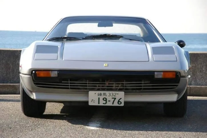 The front of the silver 308 GTB by the sea with a Japanese plate reading 19-76