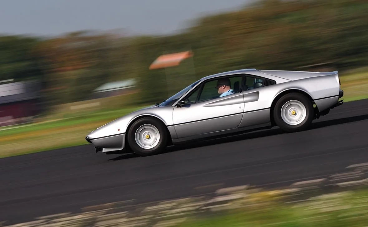 The silver 308 GTB at speed in profile, its driver visible through the window