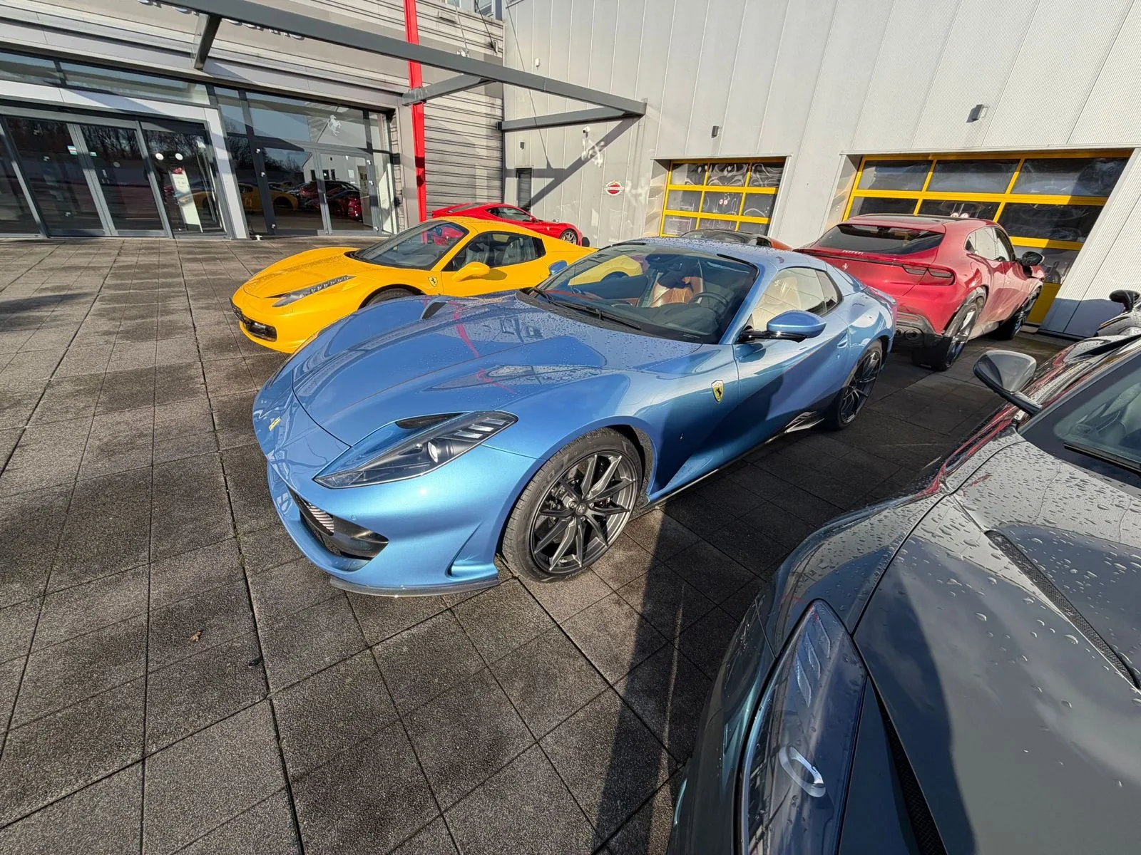 The light blue 812 GTS on the dealership forecourt beside yellow and red Ferraris