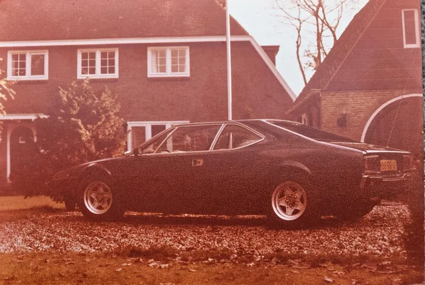 A warm-toned period photograph of the dark 308 GT4 from the side, undated
