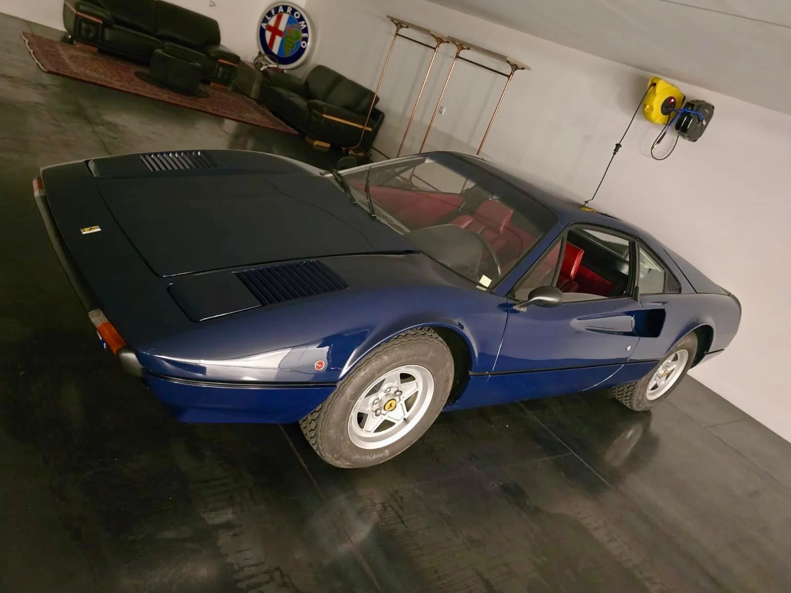 A dark blue 308 GTB with a red cabin in a workshop, seen from the front quarter